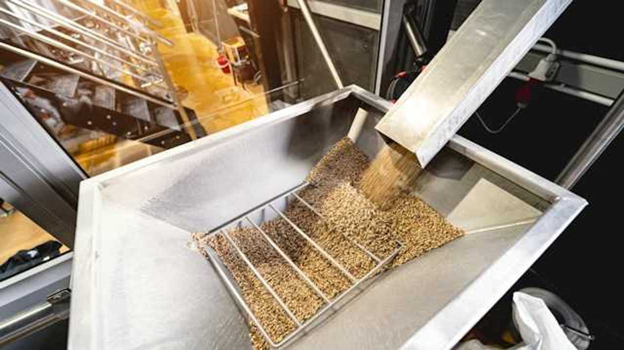 A metal chute delivering wood pellets into another metal container