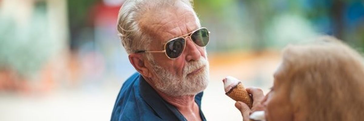A middle aged man with a white beard eating an ice cream cone on a sunny day.