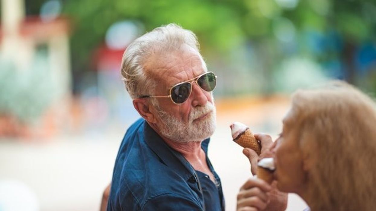 A middle aged man with a white beard eating an ice cream cone on a sunny day.