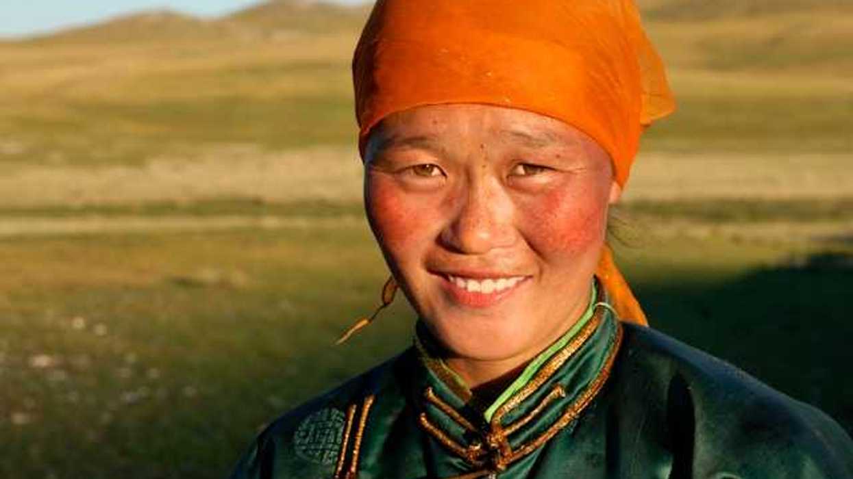 A Mongolian woman wearing an orange scarf on her head looking into the camera