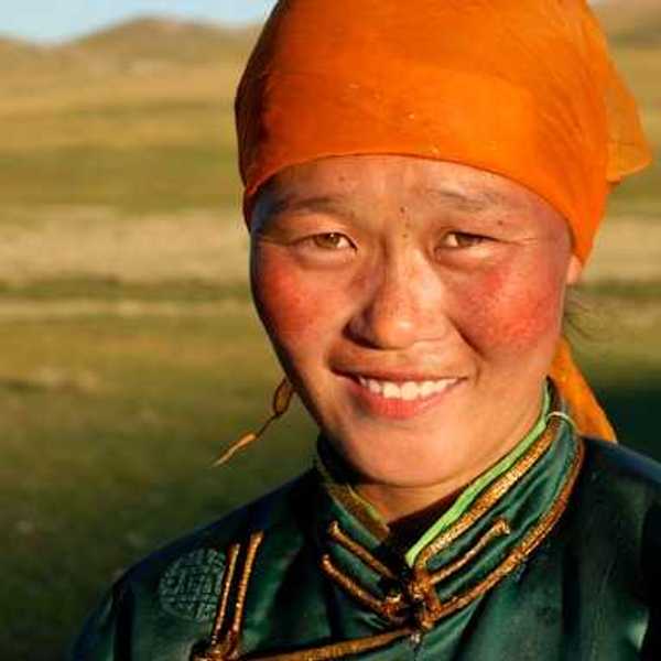 A Mongolian woman wearing an orange scarf on her head looking into the camera