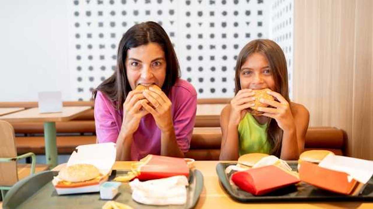A mother and daughter looking at the camera while eating fast food burgers