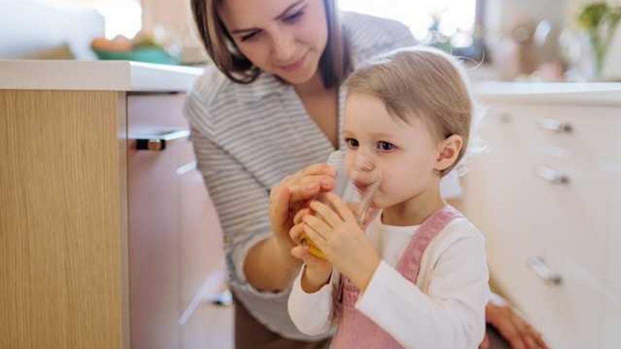 A mother helping her toddler drink a glass of water