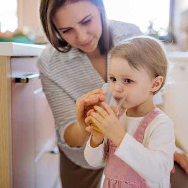 A mother helping her toddler drink a glass of water