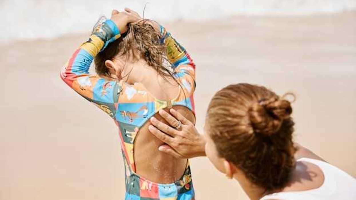 A mother rubbing sunscreen on the back of her daughter on a beach