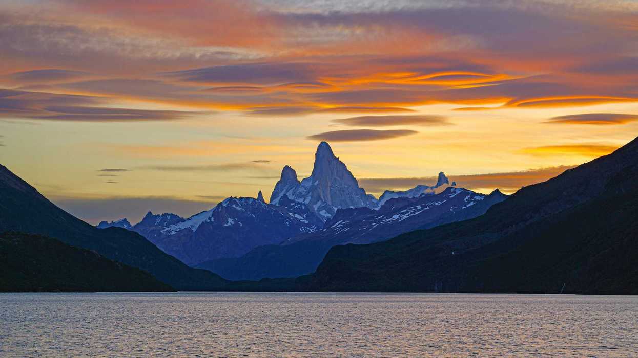 a mountain range is silhouetted against a sunset over a body of water.