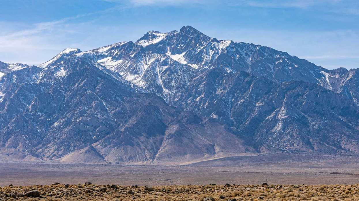 a mountain range with light snow and a desert environment in the foreground