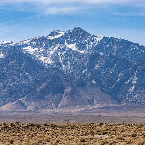 a mountain range with light snow and a desert environment in the foreground