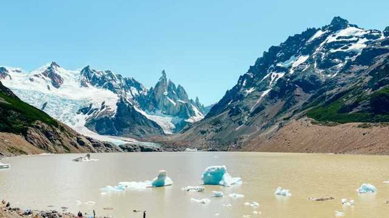 A mountain range with snow in front of a glacial lake with melting glaciers