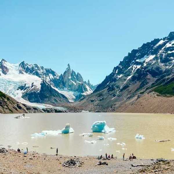 A mountain range with snow in front of a glacial lake with melting glaciers
