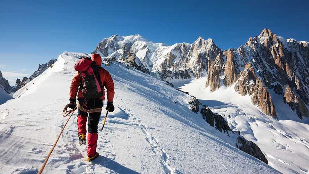 A mountaineer climbs a snowy Mont Blanc in red snow gear