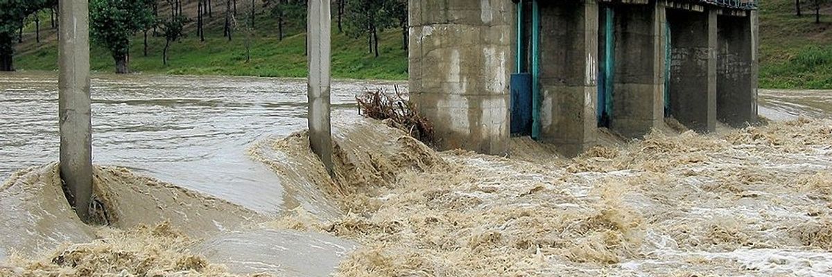 A narrow concrete bridge with fast flood waters streaming below it.