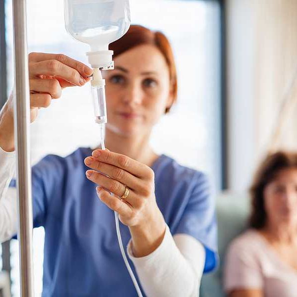 A nurse arranging an IV bag while a patient looks on