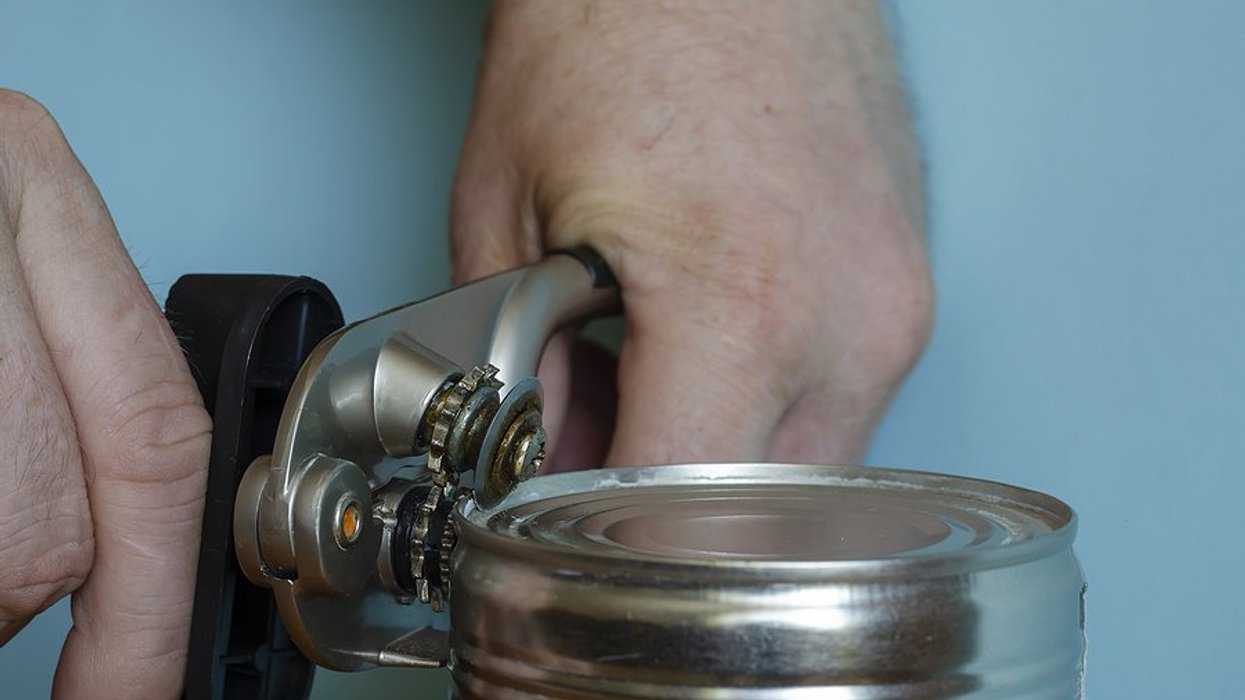 A pair of male hands with a can opener, opening a metal food can