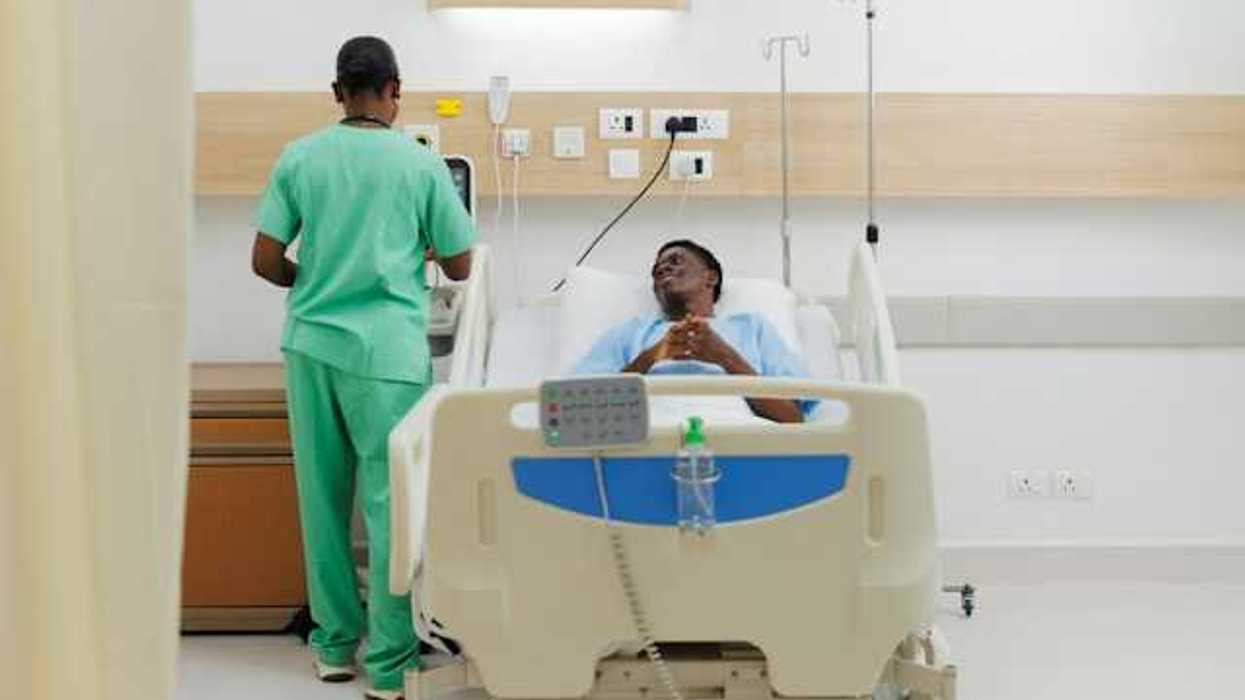A patient lying in a hospital bed looking up at a nurse in green scrubs
