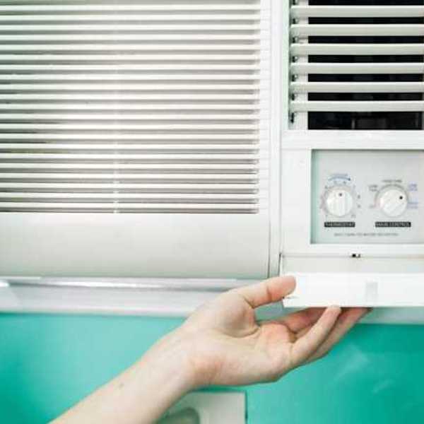 A person adjusting the controls on a window air conditioning unit