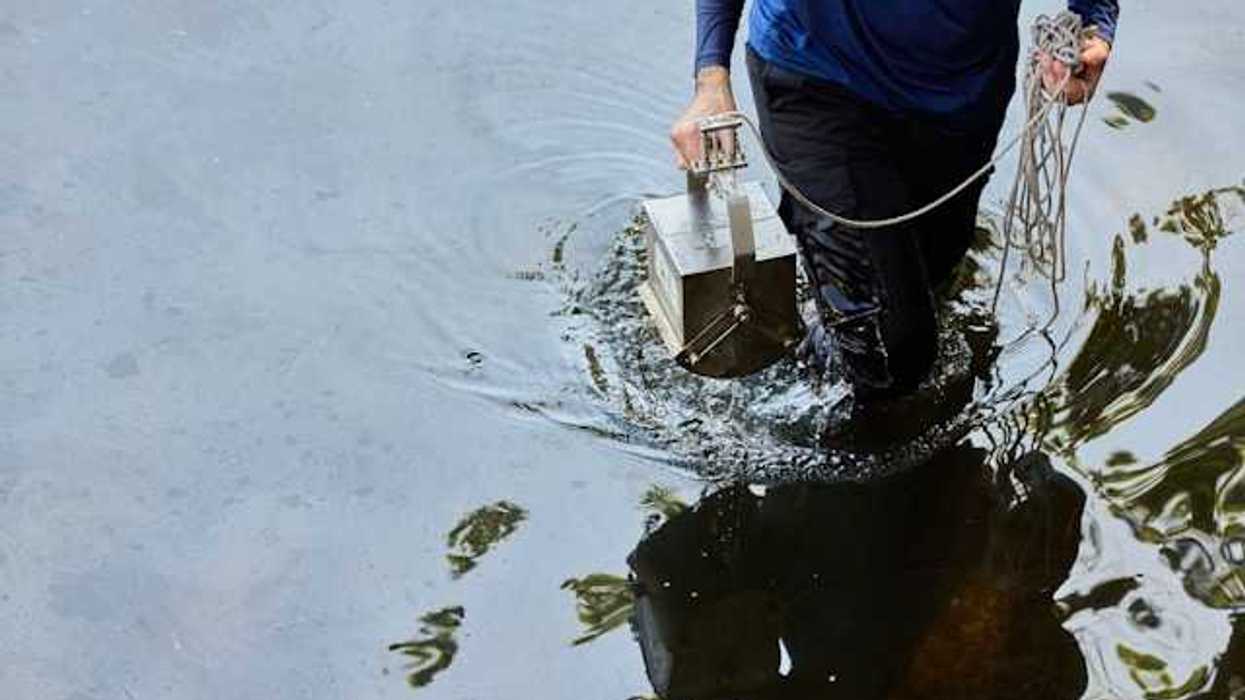 A person carrying a metal box with cord through water