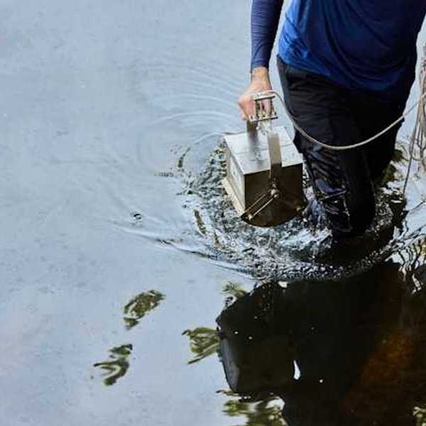 A person carrying a metal box with cord through water