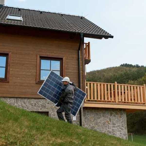 A person carrying a solar panel past a house