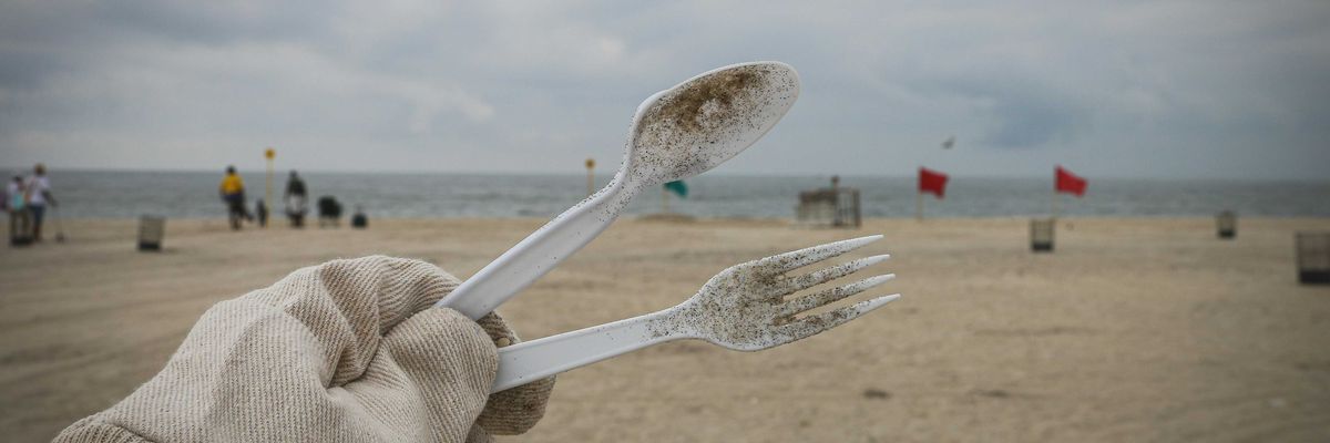 A person cleans up discarded plastic tableware on a beach