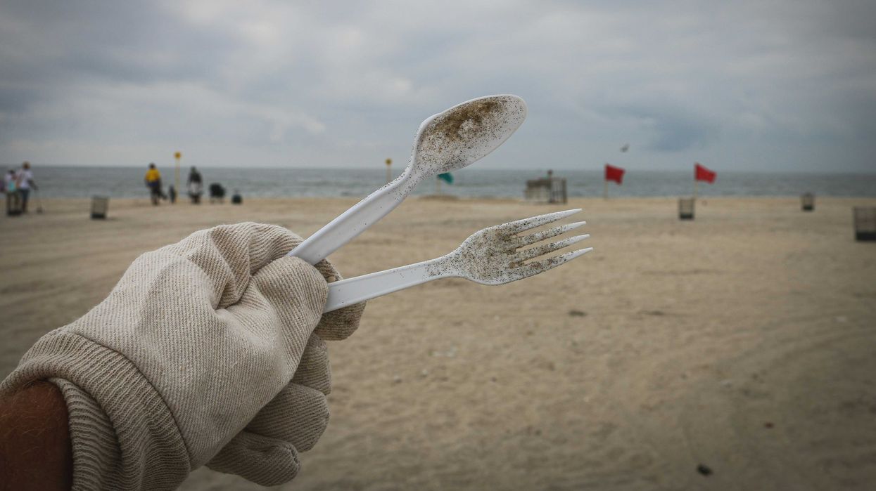 A person cleans up discarded plastic tableware on a beach