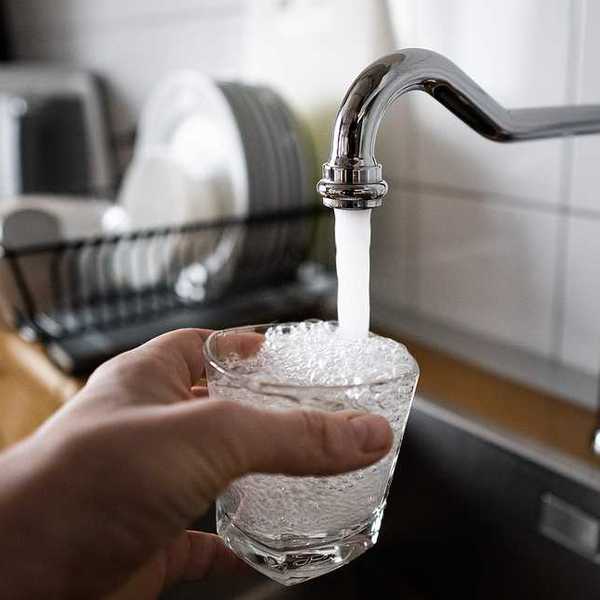 A person filling a glass of water at the kitchen sink
