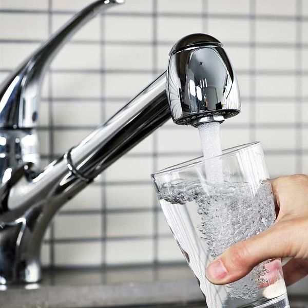A person filling a glass of water from the kitchen sink