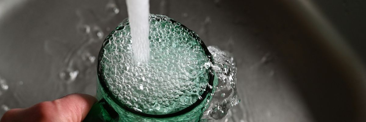 A person filling a green glass with tap water from the kitchen sink.