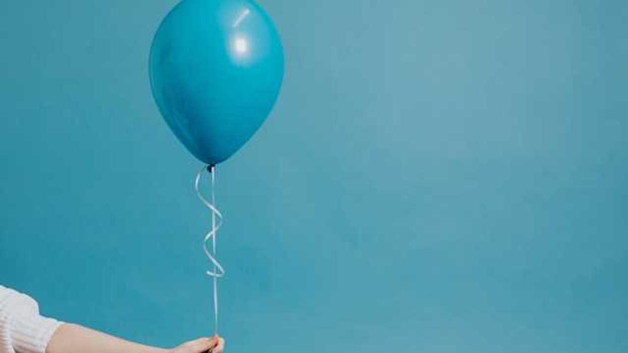 A person holding a blue balloon against a blue background