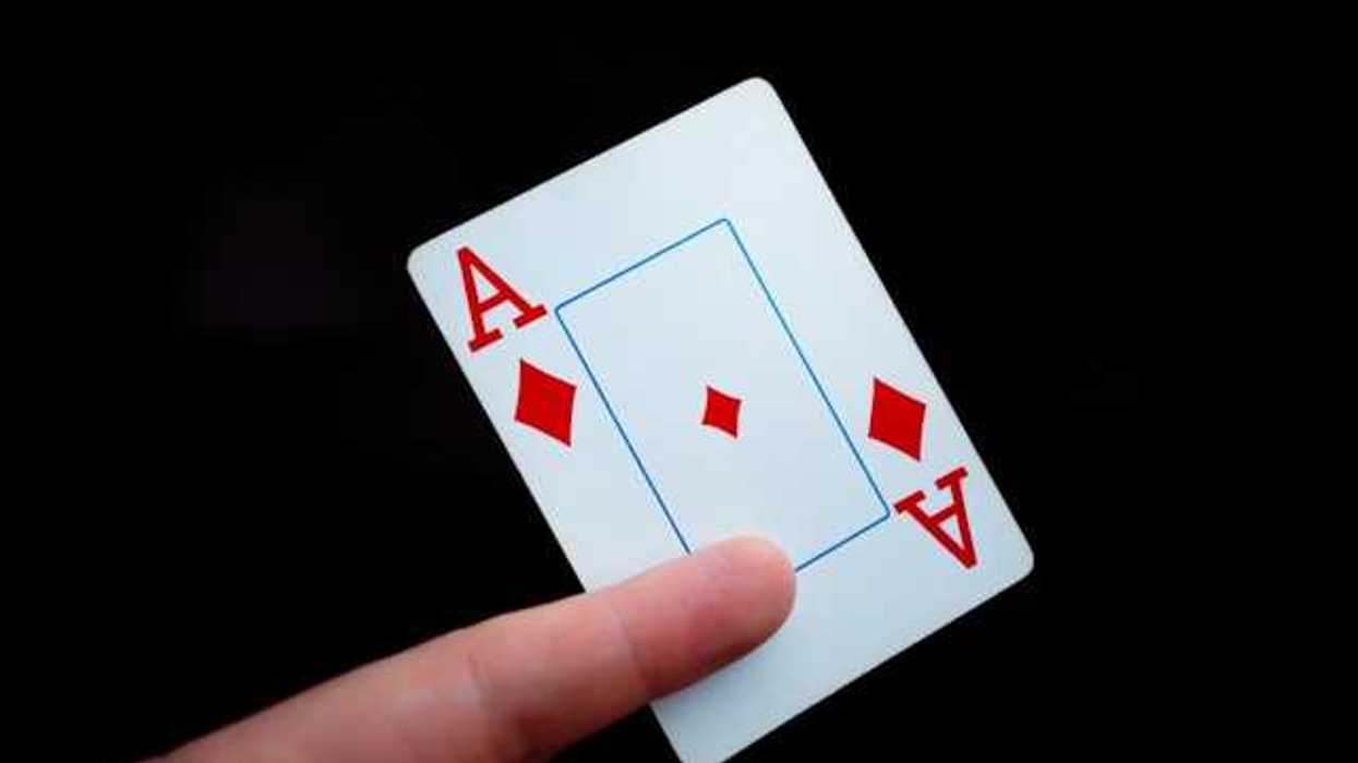 A person holding a card with the ace of diamonds on it