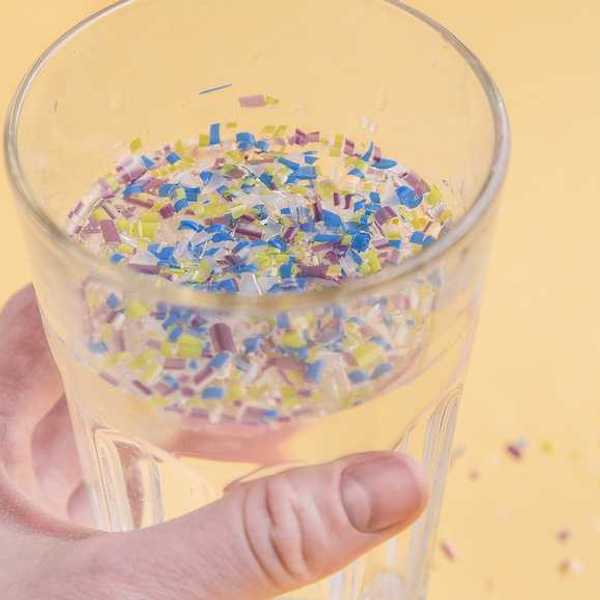 A person holding a glass of water filled with small pieces of plastic