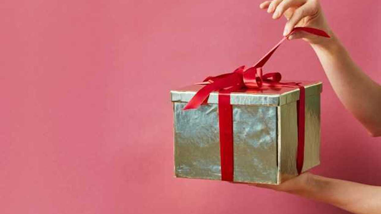 A person holding a gold-wrapped gift against a pink screen