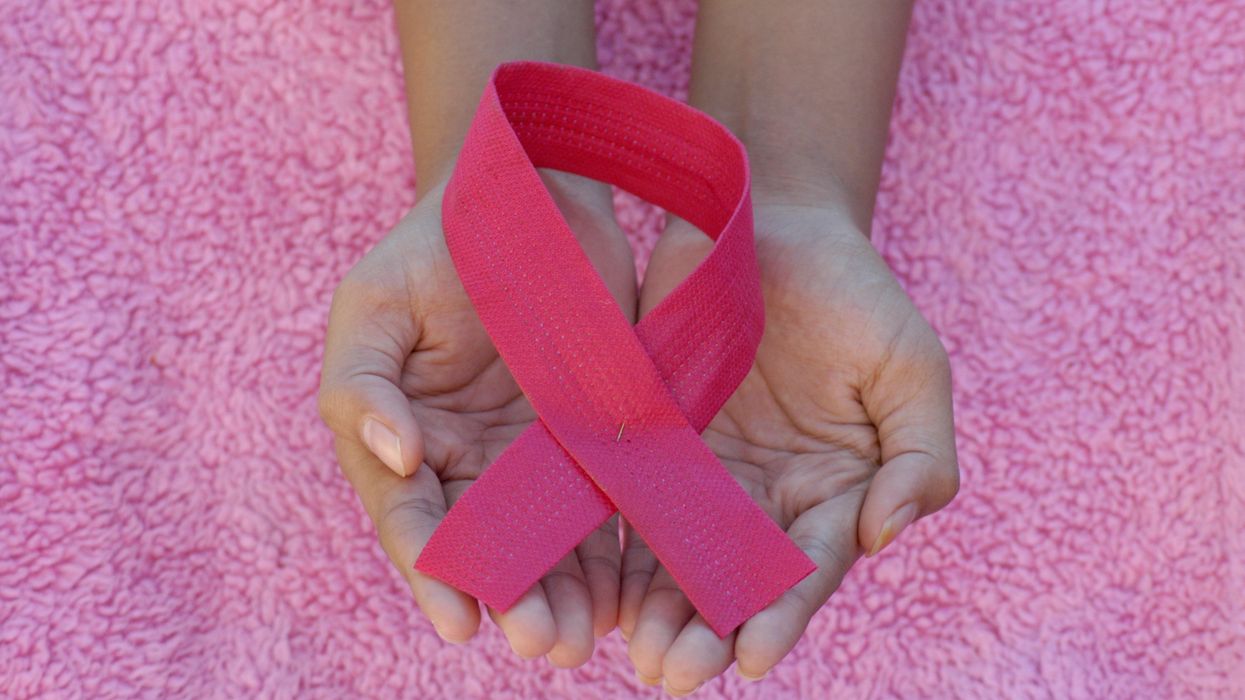 A person holding a pink ribbon in her hands against a pink background
