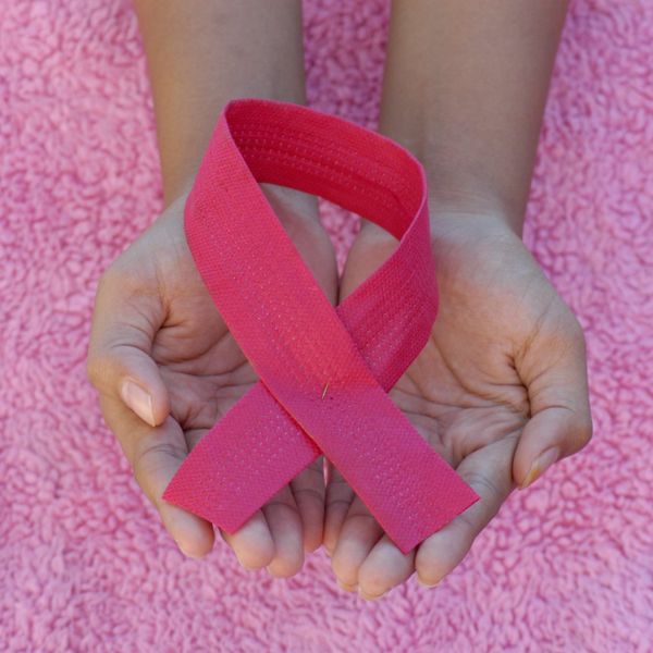 A person holding a pink ribbon in her hands against a pink background