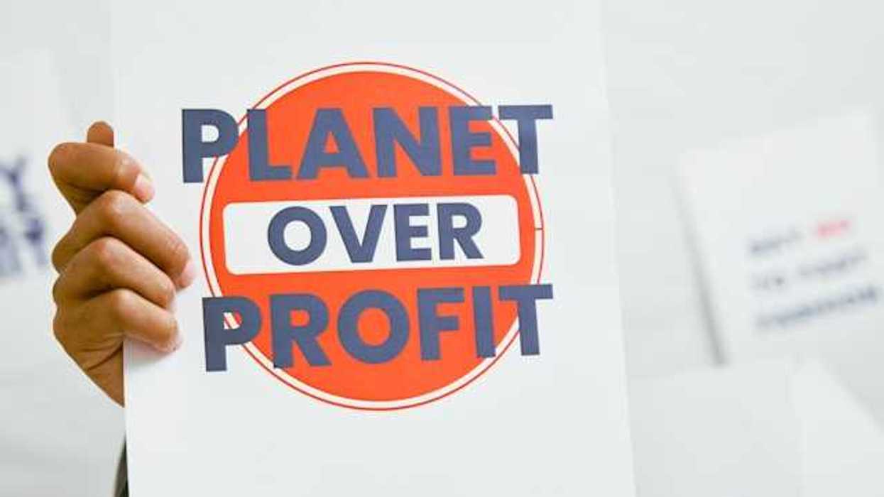A person holding a sign that says Planet Over Profit