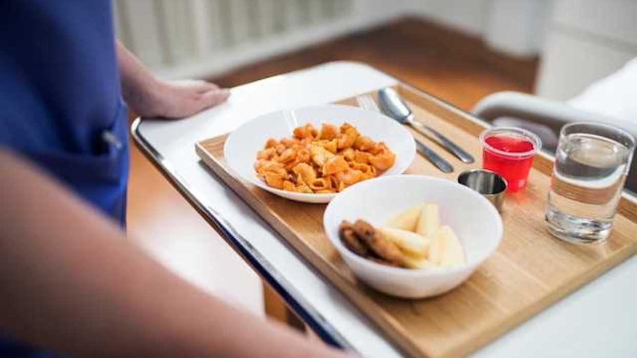 A person holding a tray with a hospital meal on it