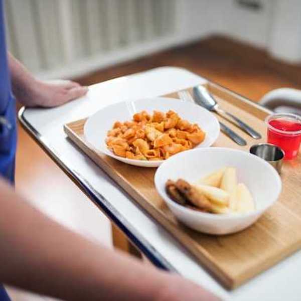 A person holding a tray with a hospital meal on it