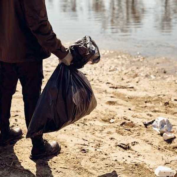 A person holding two plastic bags on a beach littered with trash