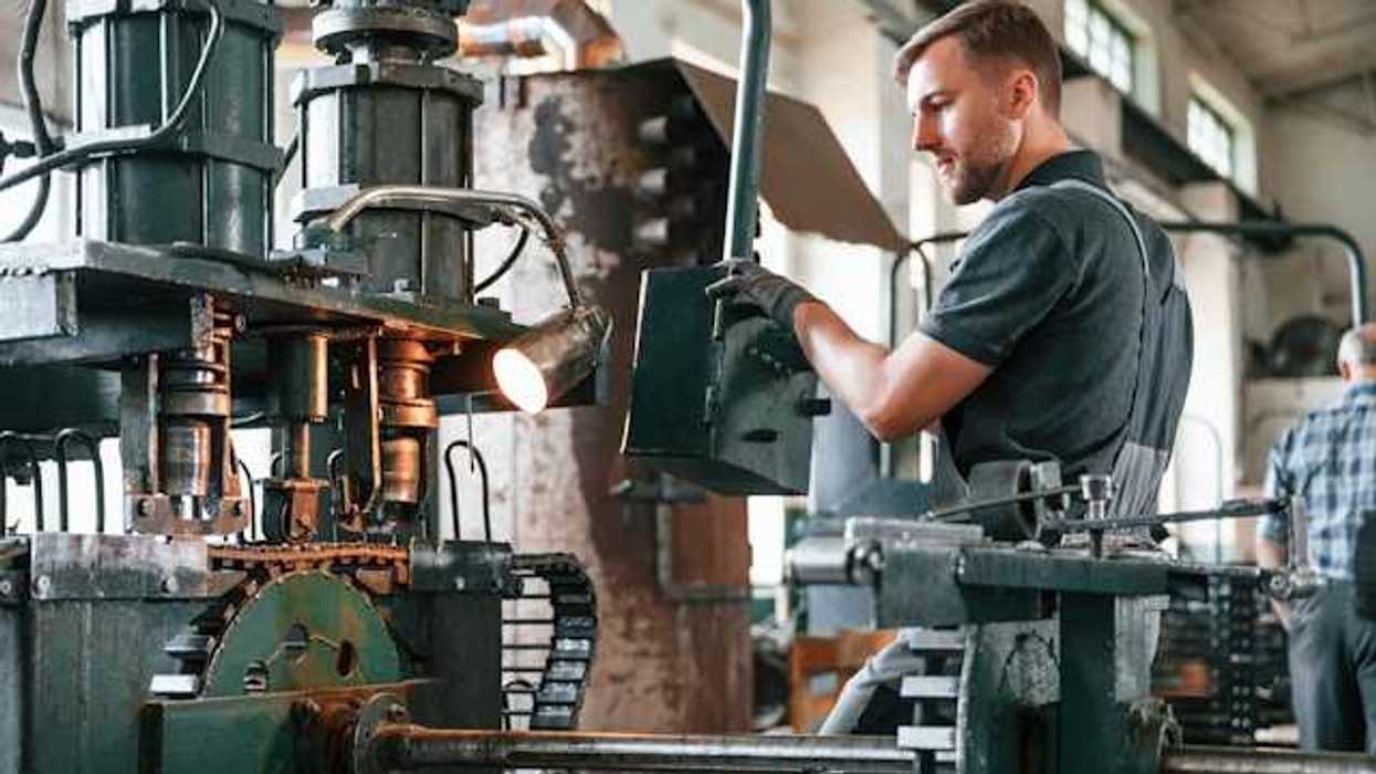 A person in a manufacturing facility standing in front of green metal equipment