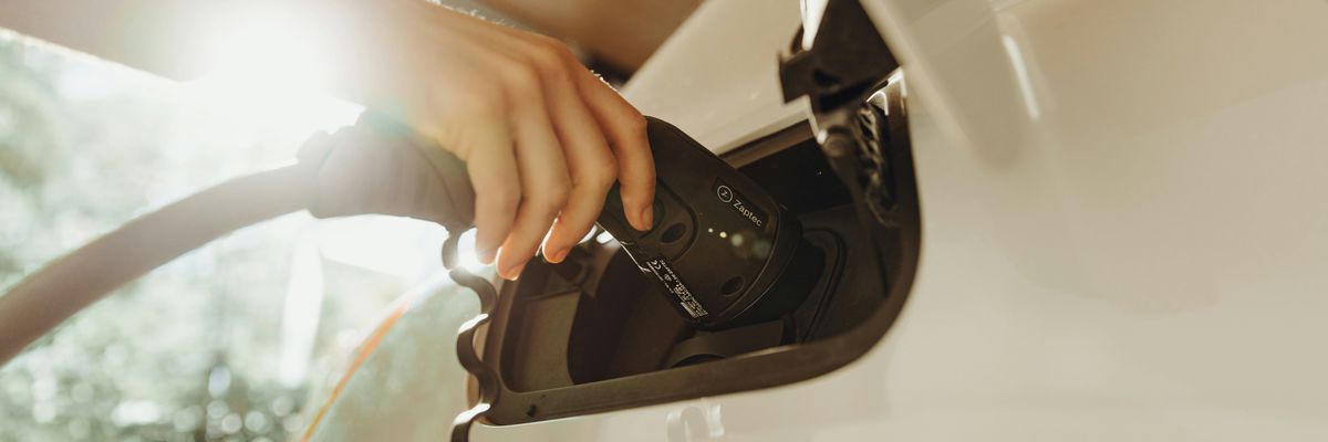 A person inserting a charger into a white electric vehicle.