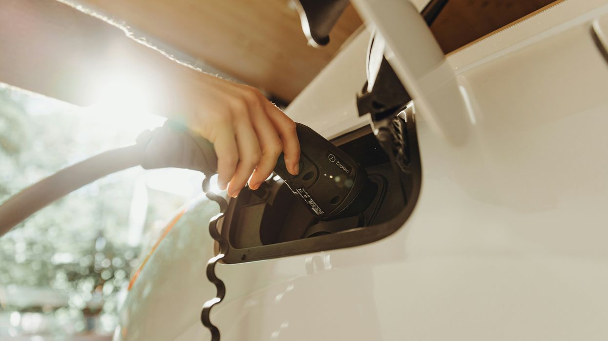 A person inserting a charger into a white electric vehicle.