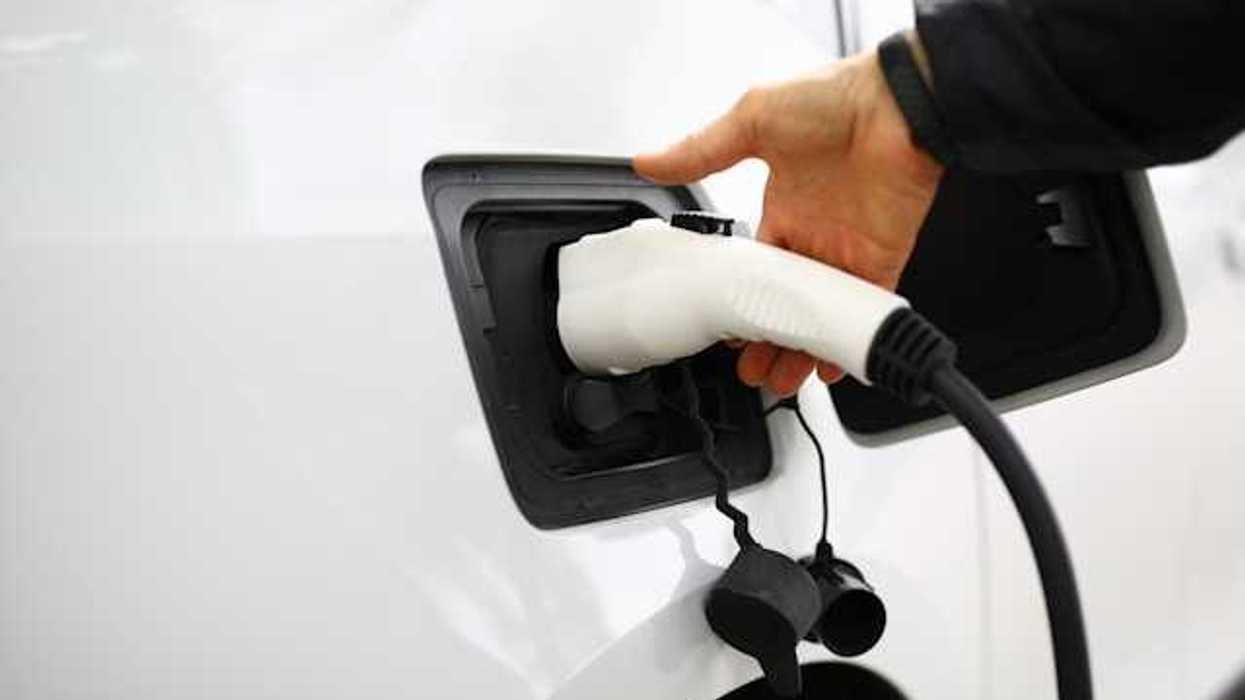 A person inserting a charger into an electric vehicle