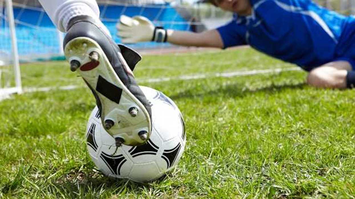 A person kicking a soccer ball into a goal