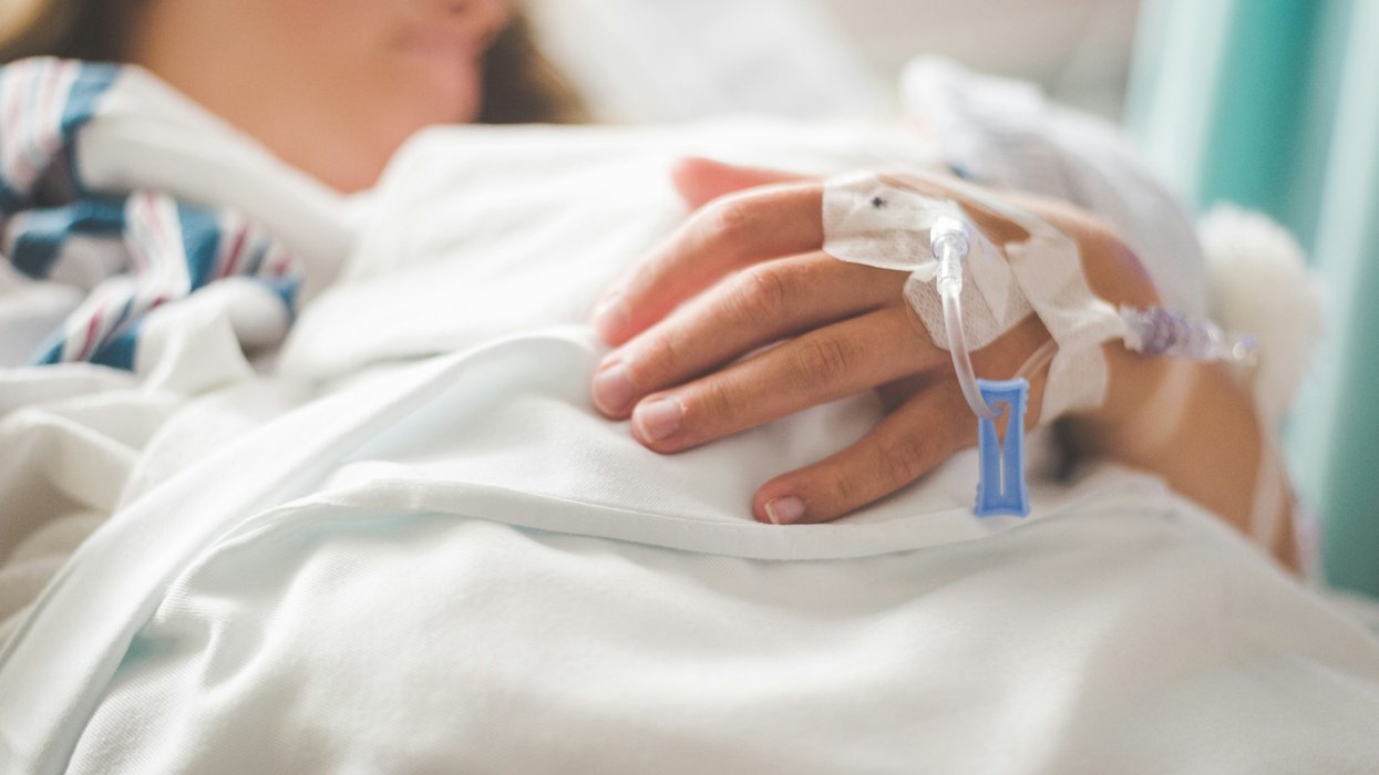 a person lies in a hospital bed with an IV