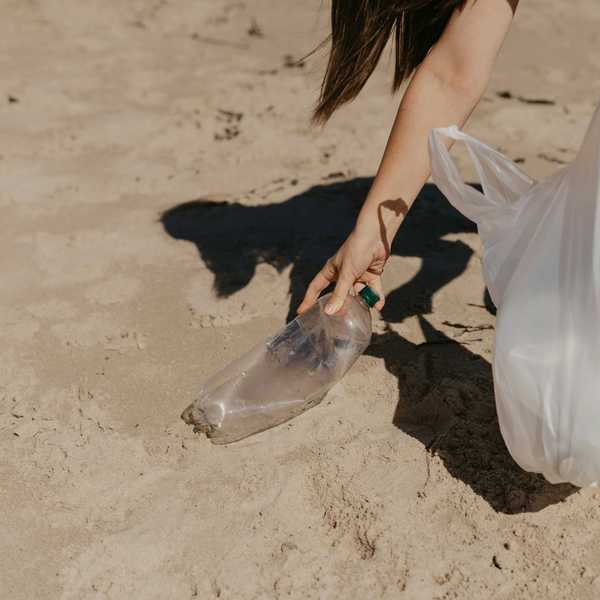 A person picking up a plastic bottle on the beach