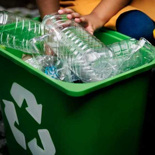 A person placing plastic bottles into a green recycling bin