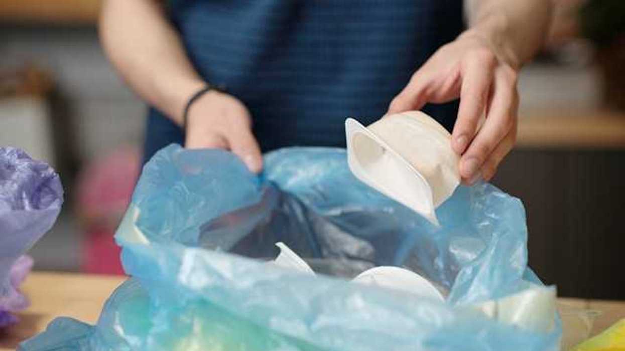 A person placing plastic single-use food containers into a plastic bag
