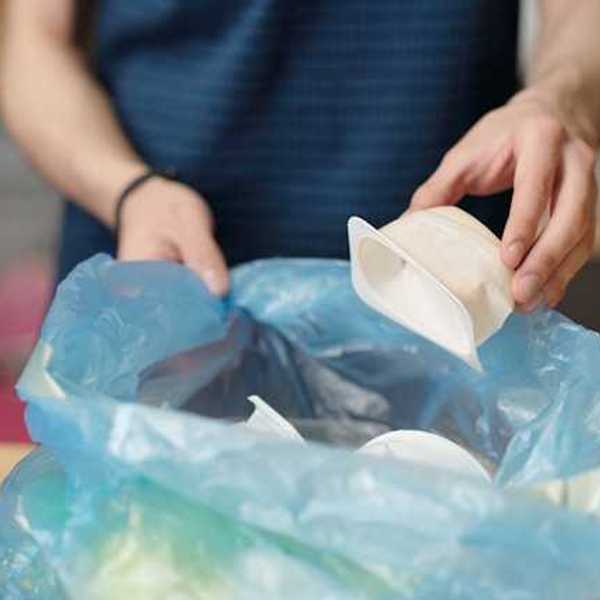 A person placing plastic single-use food containers into a plastic bag