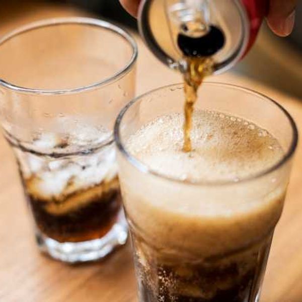 A person pouring a can of soda into a glass