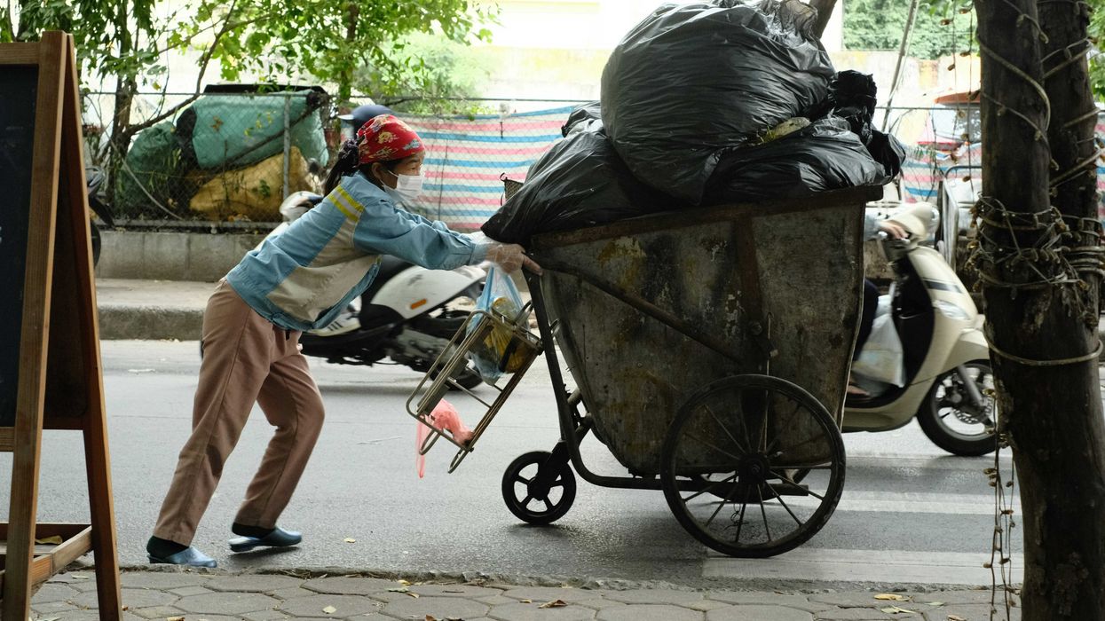A person pushes an overloaded cart filled with black plastic bags of trash.